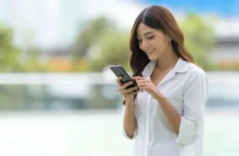 Uma mulher sorrindo e com o celular na mão.