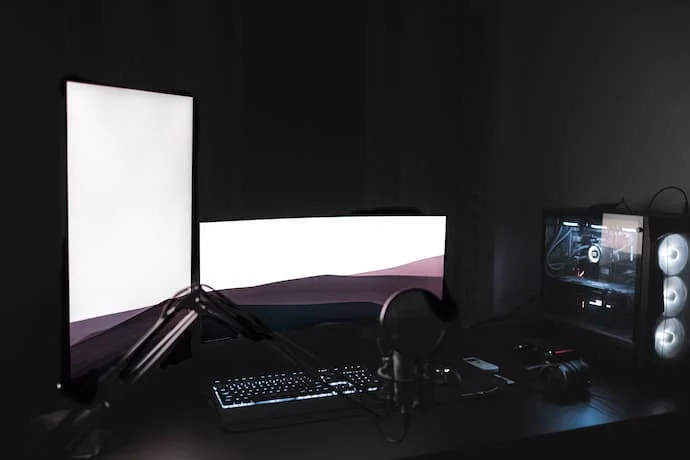 Um setup gamer escuro com telas de computadores ligadas.